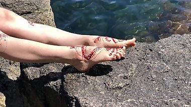 Painted henna feet resting on the rocks near the sea